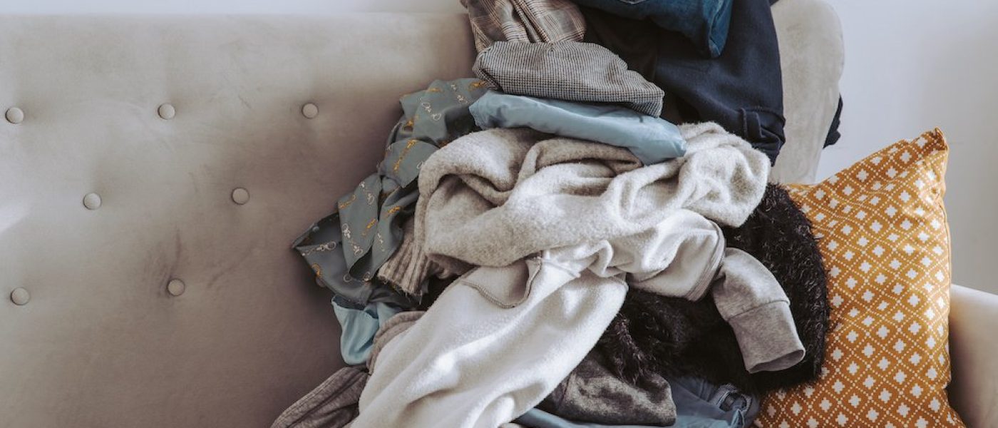 Pile of unfolded clothes for laundry on sofa. Heap of used clothes for donation and recycling. Concept of minimalism, simplicity and spring wardrobe cleaning